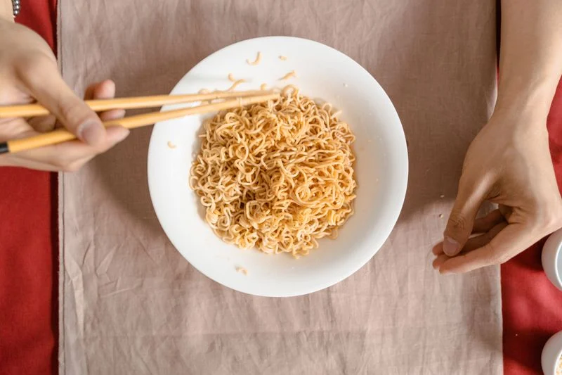Correct two-finger chopstick grip technique - hand holding chopsticks over noodle bowl - proper pinch position